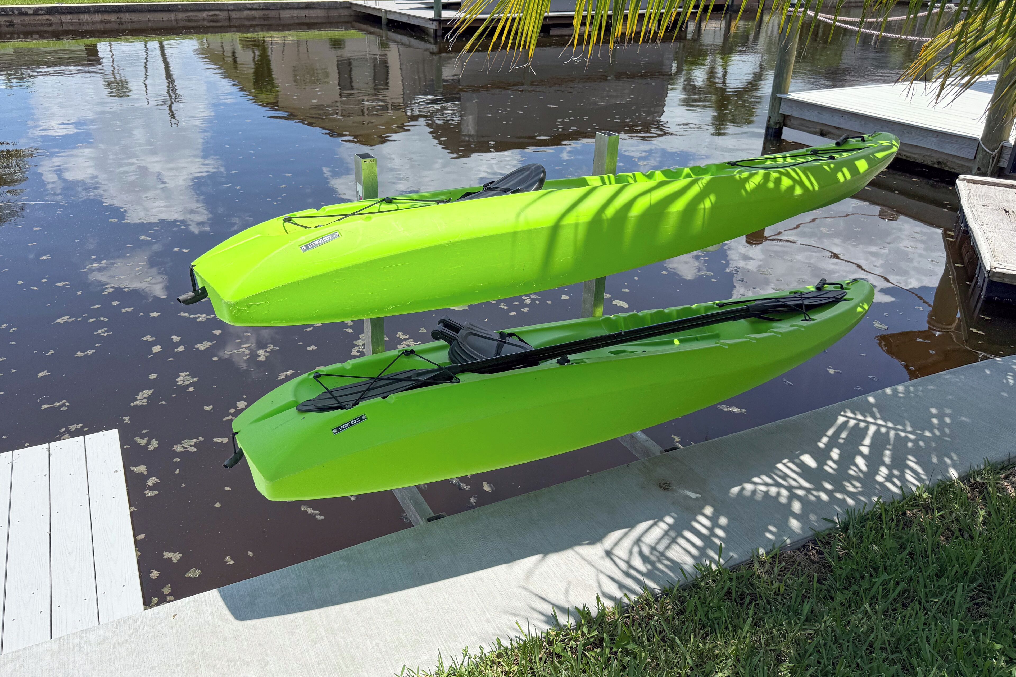 Dos kayaks verde brillante amarrados a un muelle de madera sobre aguas tranquilas.