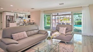 Ein modernes Wohnzimmer mit Sofa und Sesseln, einem Glastisch und Blick auf die Terrass.