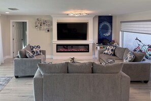 A modern living room with two grey sofas, a fireplace, a flat-screen TV, and a bicycle in the background.