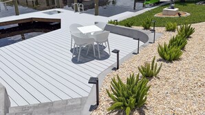 Eine Holzterrasse mit Tisch und Stühlen, einer Statue und einem kleinen Garten mit Pflanzen.