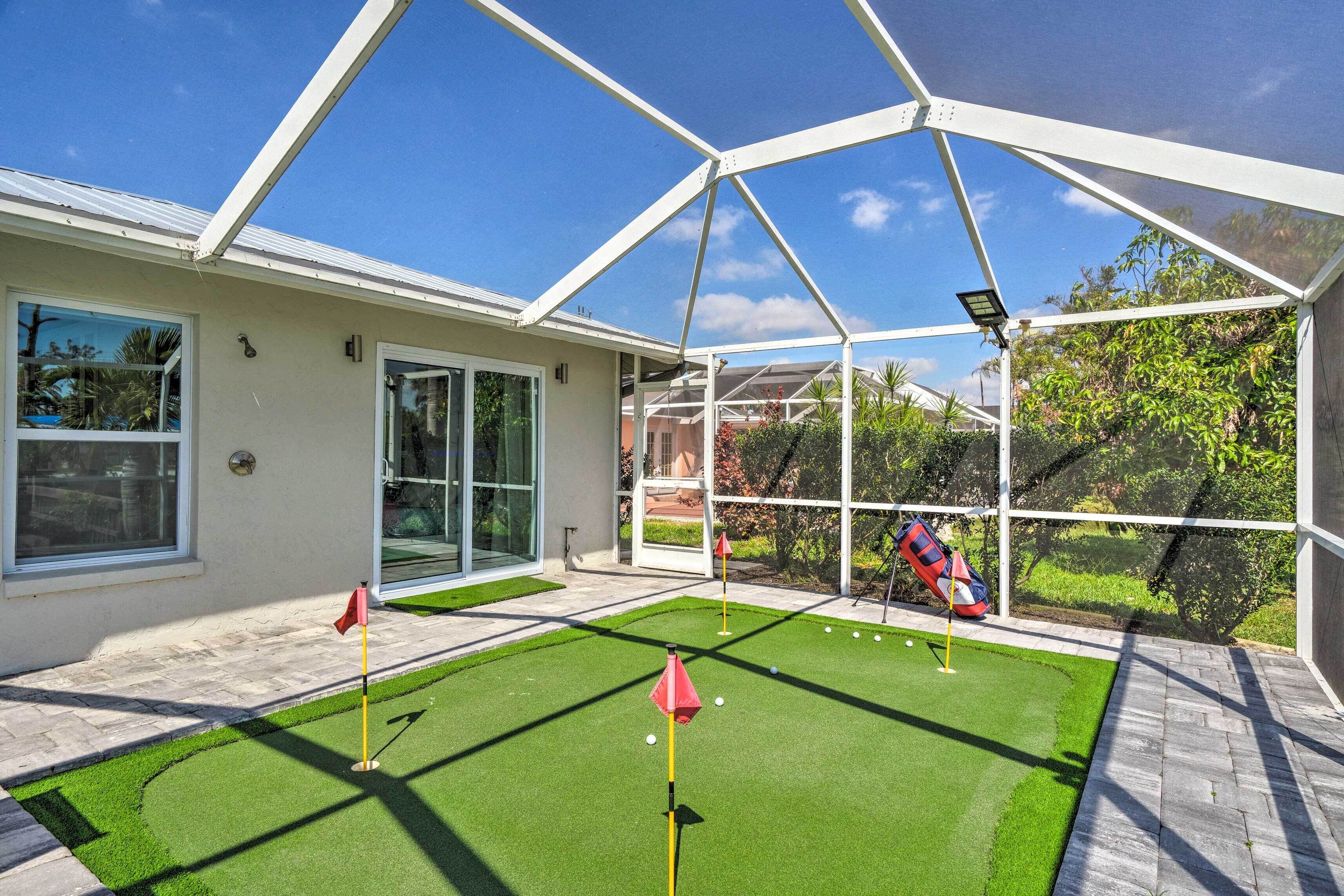 A covered outdoor area with artificial turf, a golf putting area, and a view of a residential building.