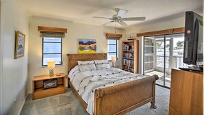 Ein Schlafzimmer mit Bett, Deckenventilator, Bücherregal, Fernseher und einem Fenster mit Jalousien.