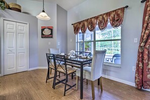 Un coin repas avec une table dressée pour quatre personnes, un luminaire suspendu et une fenêtre avec des rideaux.