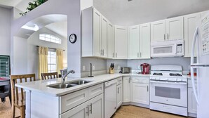 A modern kitchen with white cabinets, a sink, a microwave, a stove, and a refrigerator. - Charming Kissimmee Retreat w/ Pool & Lanai! (Kissimmee)
