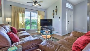 A living room with a brown leather sofa, a glass coffee table, and a flat-screen TV. - Charming Kissimmee Retreat w/ Pool & Lanai! (Kissimmee)