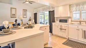 A modern kitchen with white cabinetry, a central island, and a dining area with blue chairs. - Chic Cape Coral Oasis w/ Pool: 5 Mi to Beach! (Cape Coral)