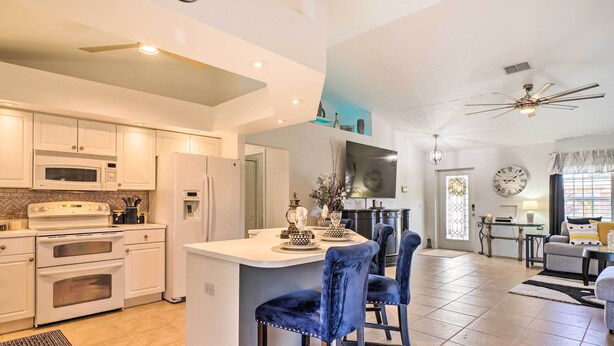 A modern kitchen with white cabinetry, a central island with bar stools, and a dining area with a chandelier. - Chic Cape Coral Oasis w/ Pool: 5 Mi to Beach! (Cape Coral)