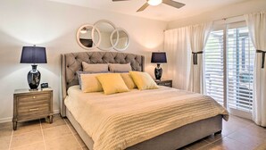 A bedroom with a large bed, two bedside tables with lamps, a ceiling fan, and a window with curtains. - Chic Cape Coral Oasis w/ Pool: 5 Mi to Beach! (Cape Coral)