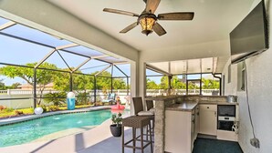 A covered outdoor kitchen area with a pool, a ceiling fan, and a view of the surrounding landscape. - Chic Cape Coral Oasis w/ Pool: 5 Mi to Beach! (Cape Coral)