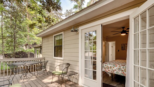A wooden deck with a table and chairs, a bed with a floral bedspread, and a ceiling fan in a room with a door leading outside. - Charming Tallahassee Townhouse ~ 3 Mi to Fsu! (Tallahassee)