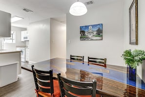A modern dining area with a glass-top table, black chairs, a white wall with a framed picture, and a potted plant. - Charming Tallahassee Townhouse ~ 3 Mi to Fsu! (Tallahassee)
