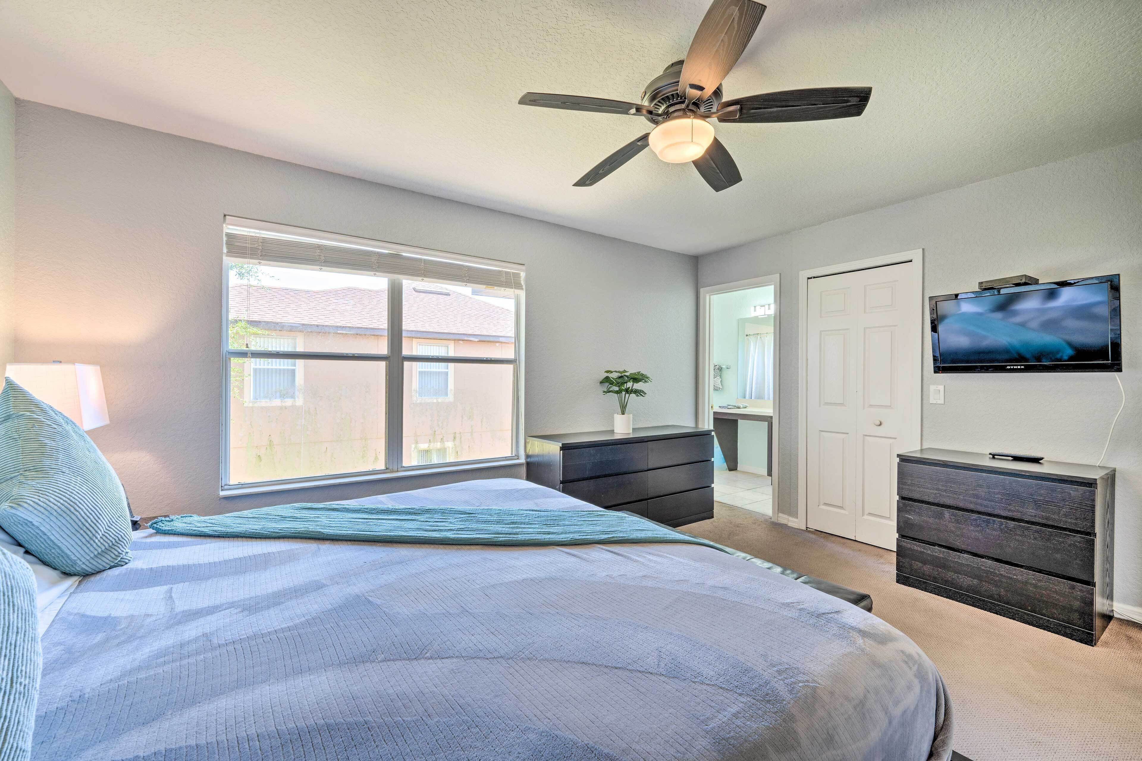 A bedroom with a bed, a ceiling fan, a TV, and a window.