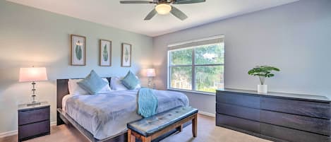 A bedroom with a bed, bedside tables, a bench, a ceiling fan, a window, and a dresser.