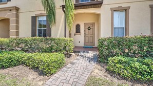 A two-story building with a brick pathway leading to a door with a wreath. - Chic Resort Townhome ~ 9 Mi to Disney Parks! (Davenport)