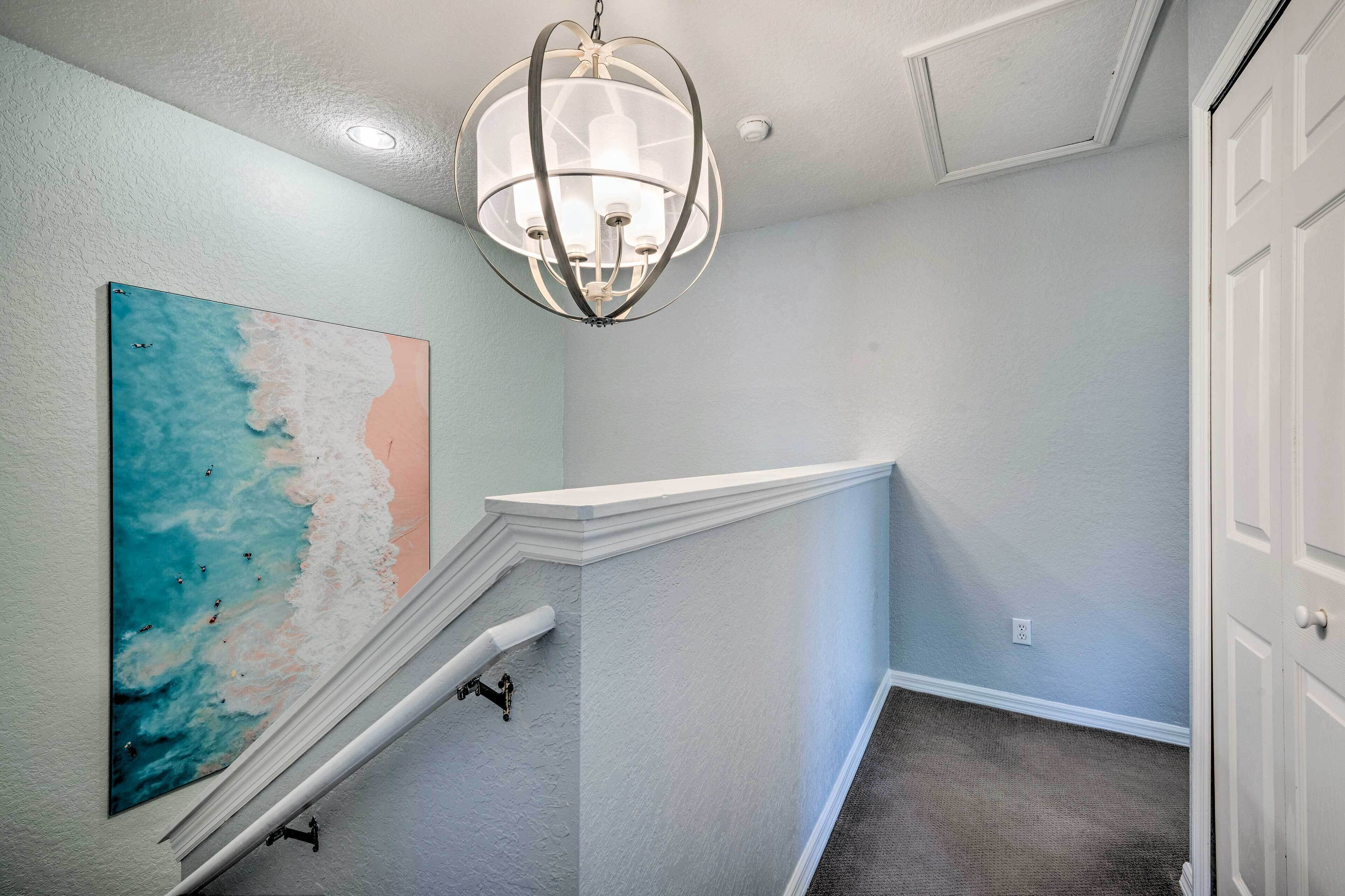 A hallway with a staircase, a wall-mounted painting, and a ceiling light fixture.