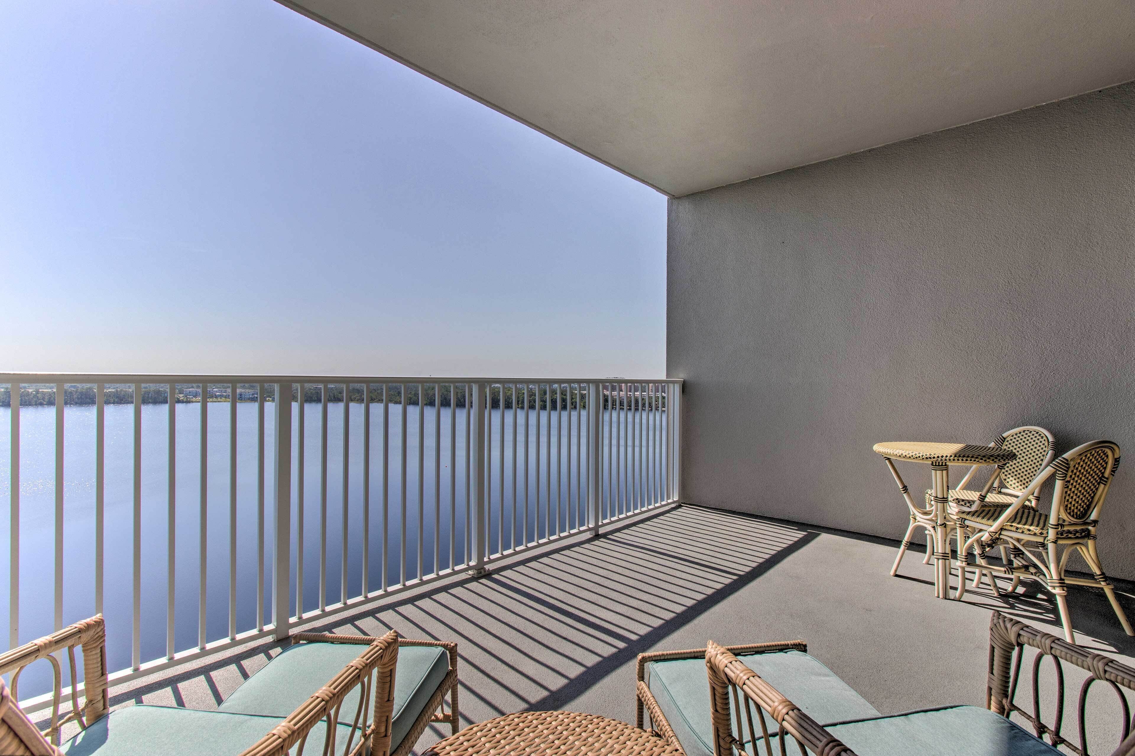 A balcony with a view of a lake, wicker furniture, and a railing.