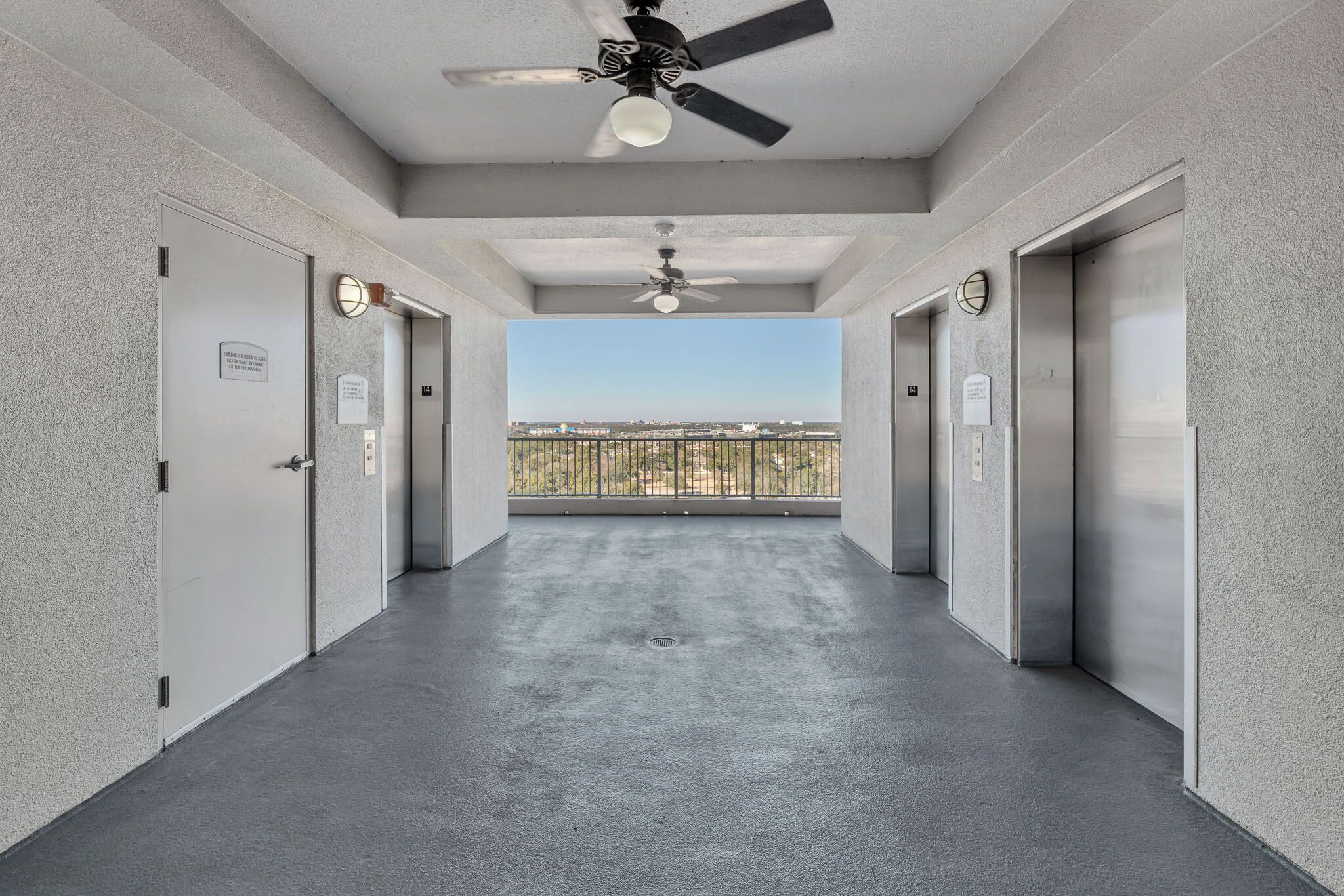A corridor with two elevators, a ceiling fan, and a view of a balcony with a railing.