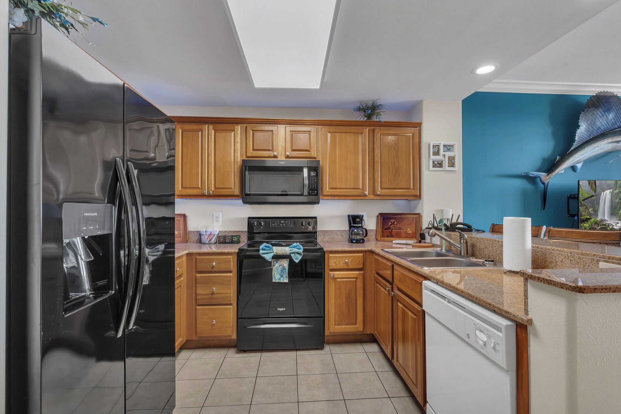 A modern kitchen with wooden cabinets, a black refrigerator, a microwave, an oven, and a dishwasher.