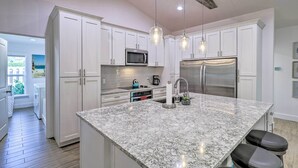 Cozinha moderna com armários brancos, bancada de granito, eletrodomésticos de aço inoxidável e iluminação pendente.