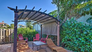 Uma área de estar coberta ao ar livre com espreguiçadeiras e cadeiras de madeira, uma mesa e uma estrutura de pérgola.