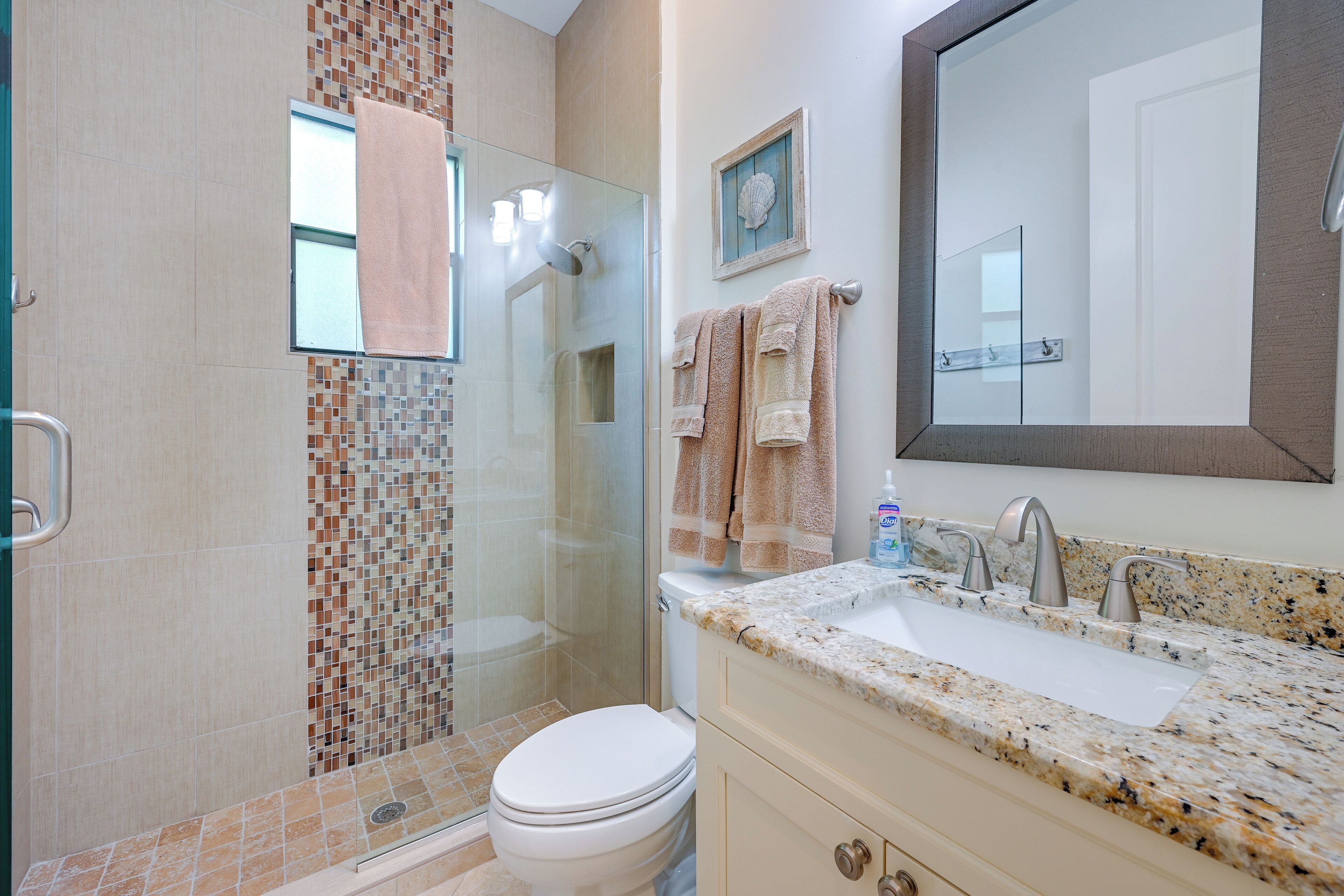 A modern bathroom with a glass shower enclosure, a white toilet, a granite countertop sink, and a large mirror.