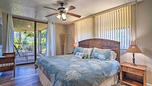 Un dormitorio con cama, mesita de noche, ventilador de techo, ventana con persianas y balcón con sillas.