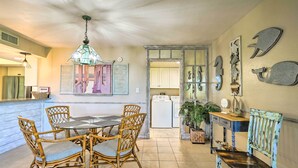 Un comedor con una mesa redonda y sillas de mimbre, una cocina con electrodomésticos blancos, y decoración en las paredes.