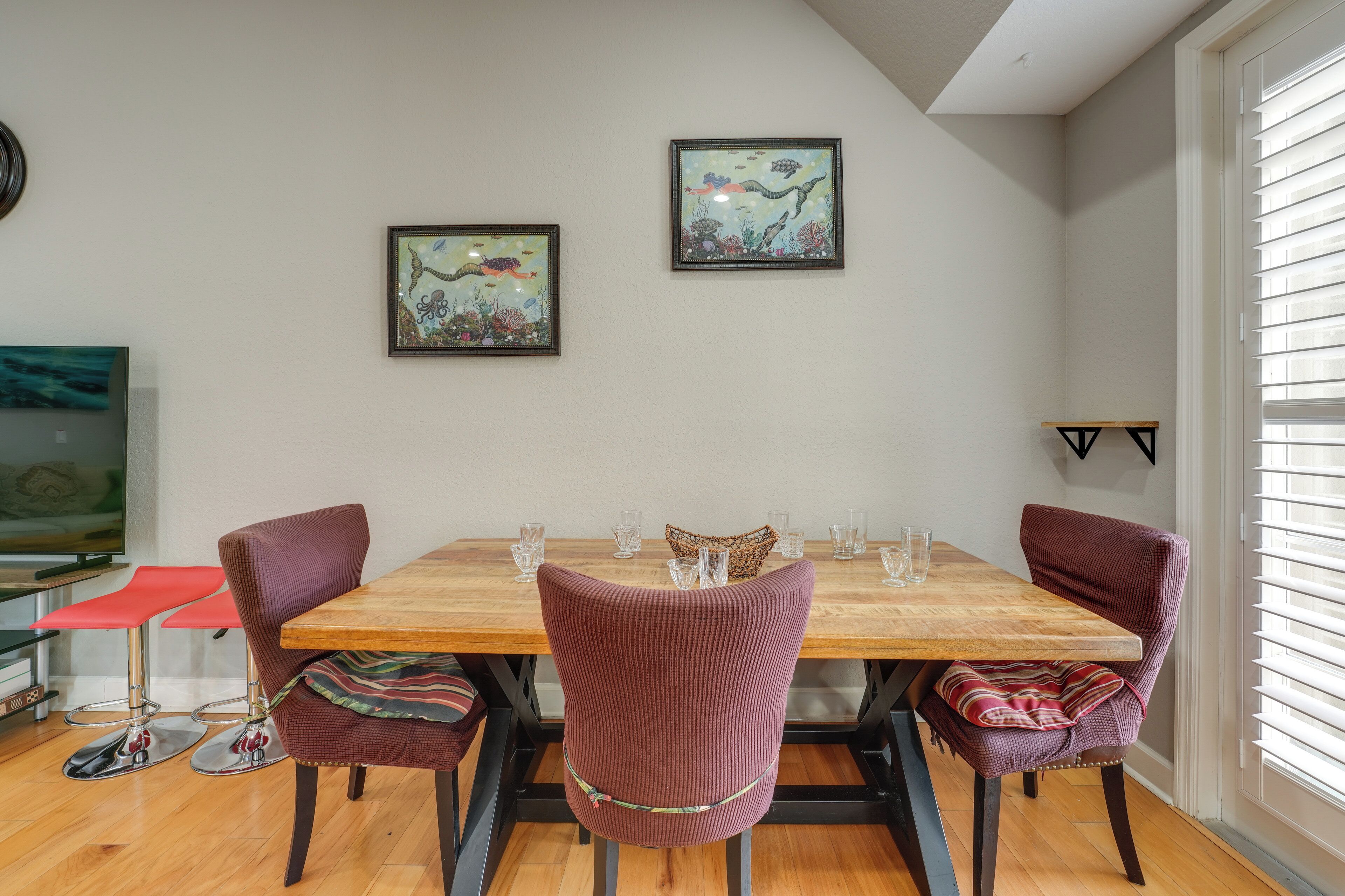 A dining area with a wooden table, four chairs, and two framed pictures on the wall.