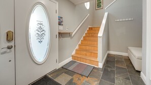A hallway with a wooden staircase, a white door with a decorative glass panel, and a small shelf with items on the wall. - Coastal 'sea Side' Townhome - Walk to Beach! (Clearwater Beach)