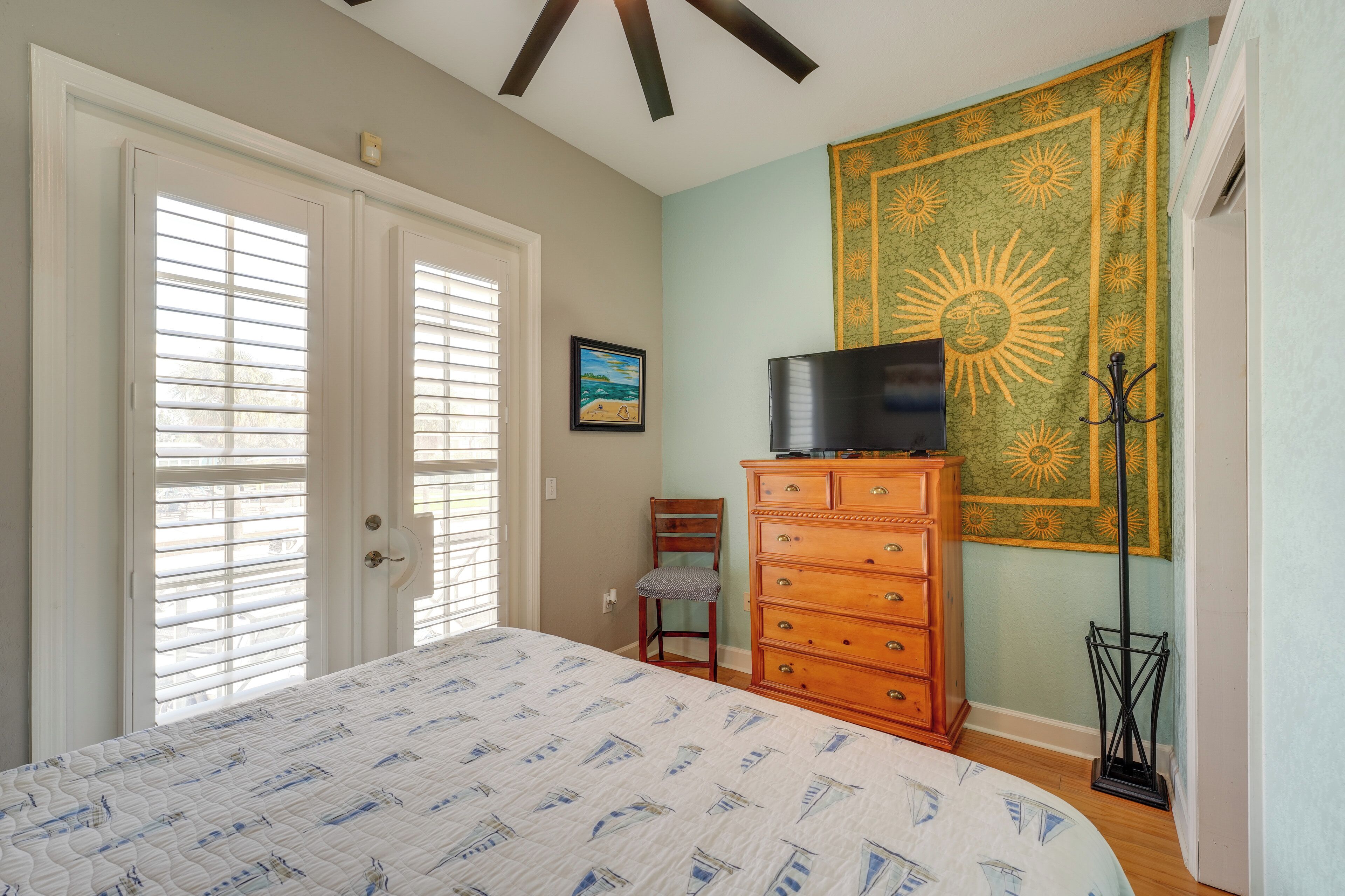 A bedroom with a bed, a dresser, a chair, a tapestry, and a television.