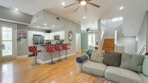 A spacious living area with a wooden floor, a sofa with multiple cushions, a kitchen area with a bar, and a staircase leading to an upper level. - Coastal 'sea Side' Townhome - Walk to Beach! (Clearwater Beach)