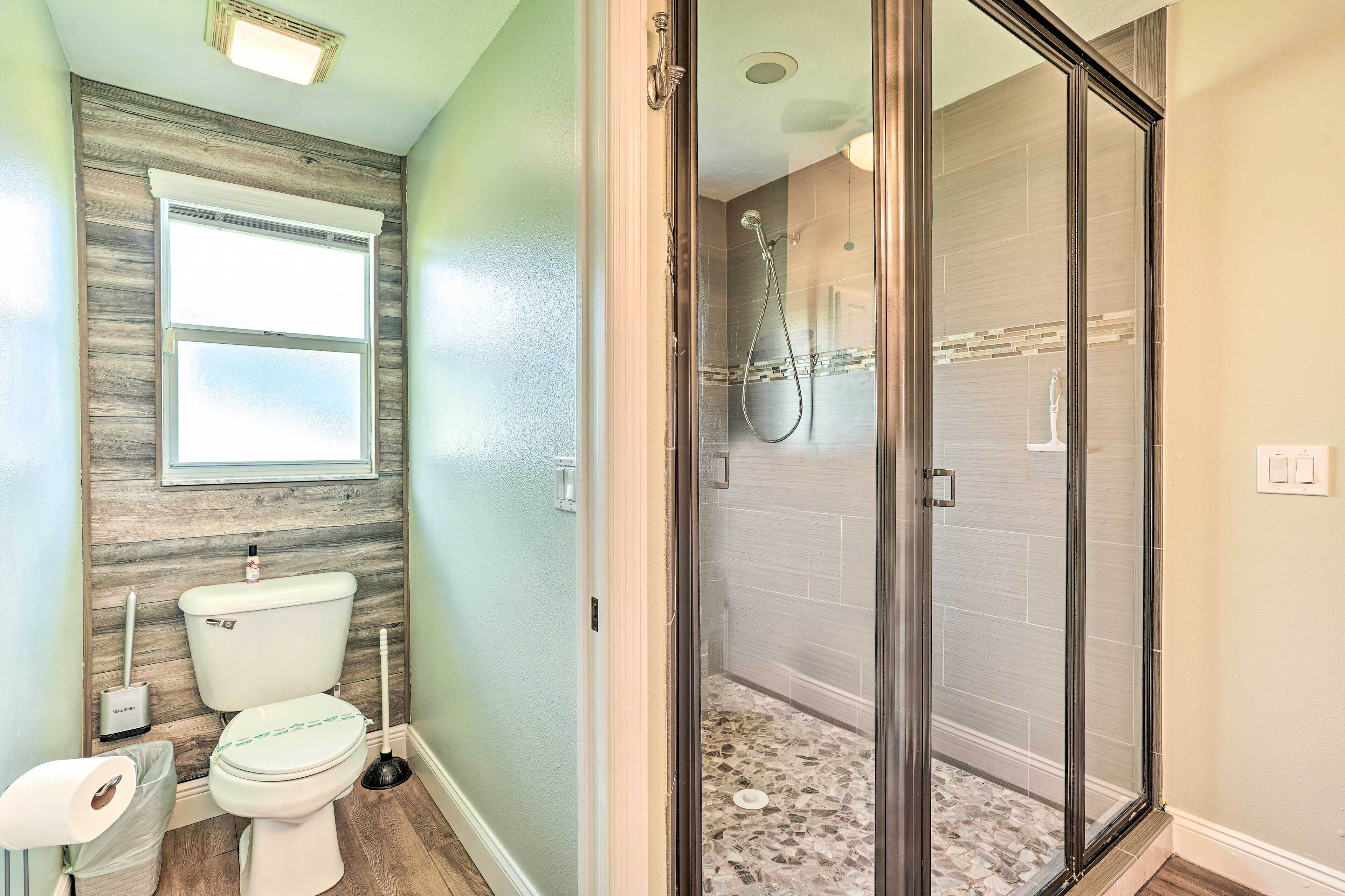 Une salle de bain comprenant des toilettes, un bidet, une douche avec une porte en verre et une fenêtre située au-dessus des toilettes.
