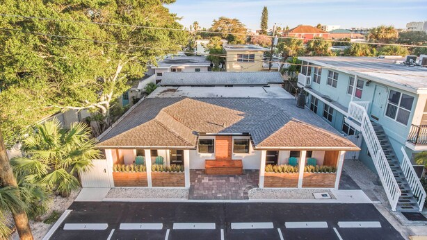 A two-story building with a tiled roof, a covered patio, and a parking lot with marked spaces. - 2 Conjoined Units - Steps From Madeira Beach! (Madeira Beach)