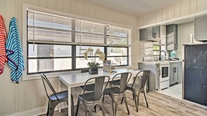 A kitchen with a dining area, featuring a white table, four chairs, a window with blinds, and a stove. - 2 Conjoined Units - Steps From Madeira Beach! (Madeira Beach)