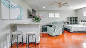 Une chambre moderne comprenant un lit, un bureau, deux tabourets de bar, une chaise et un ventilateur de plafond.