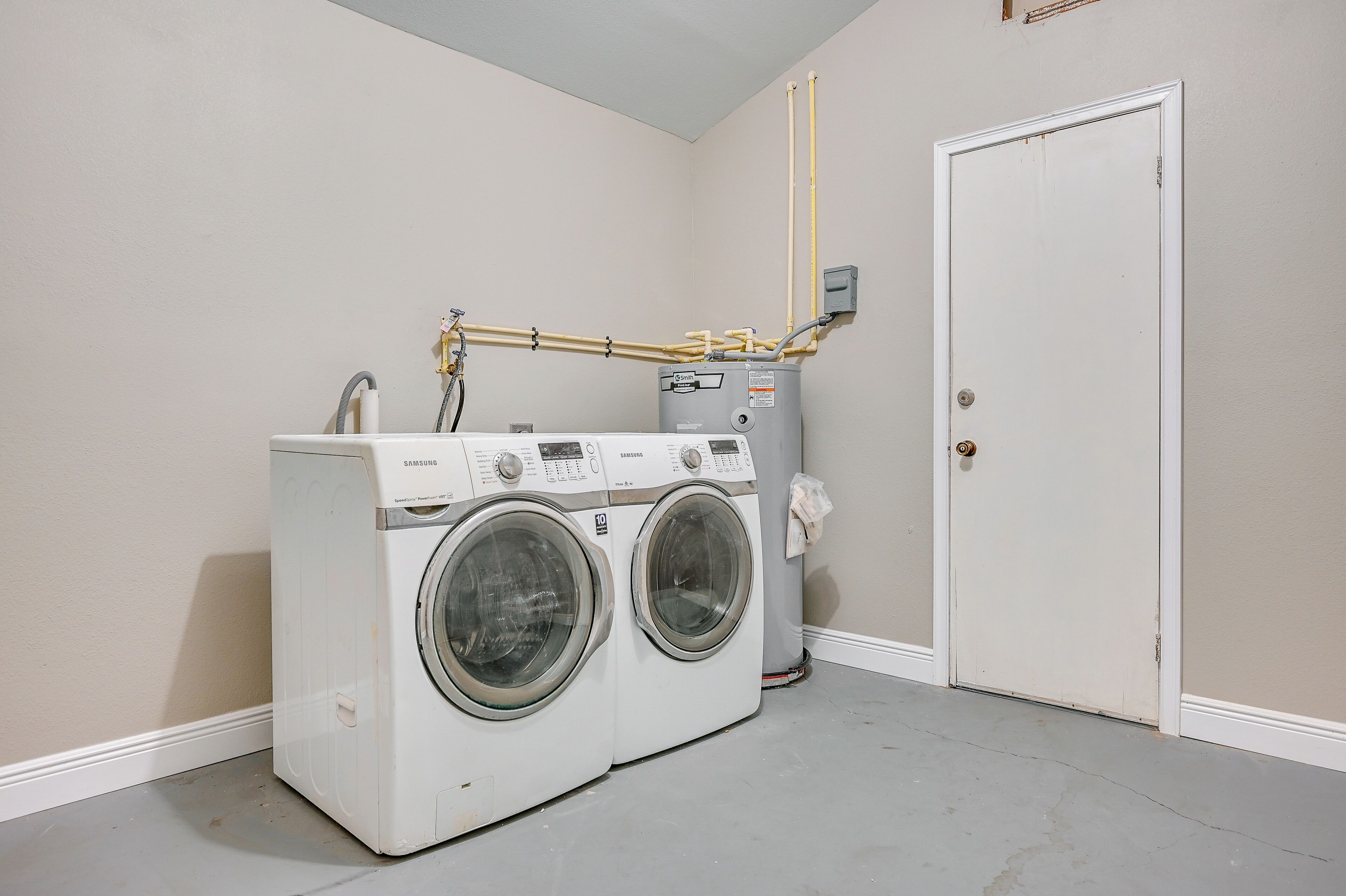A laundry room with two white front-loading washers and dryers, a water heater, and a door.