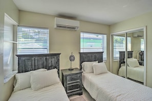 A bedroom with two beds, a nightstand, an air conditioning unit, and a large mirror. - Cozy Key West Beach Cottage: Walk to Beaches! (Key West)