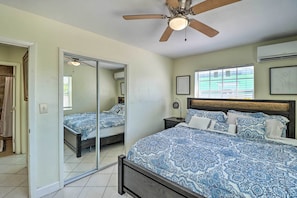 A bedroom with a large bed, a ceiling fan, a window with blinds, and a door leading to another room. - Cozy Key West Beach Cottage: Walk to Beaches! (Key West)