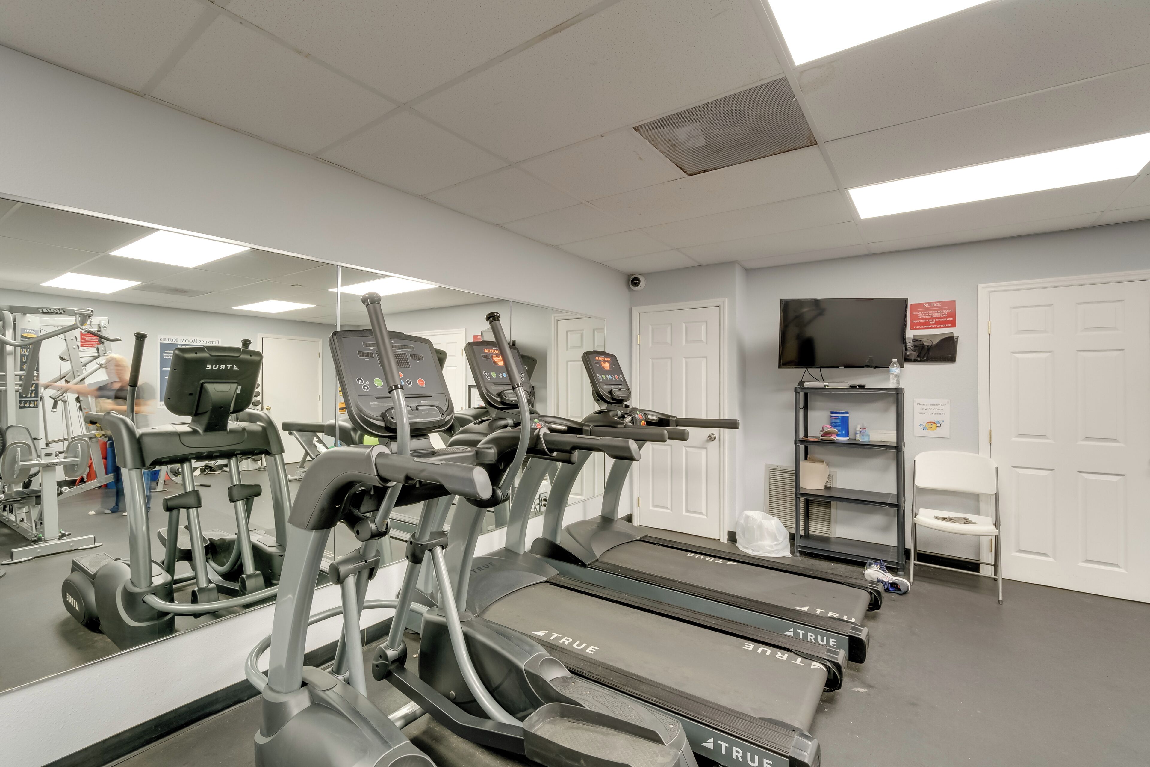 Une salle de sport équipée de tapis de course, de vélos d’exercice et d’un mur recouvert de miroirs.
