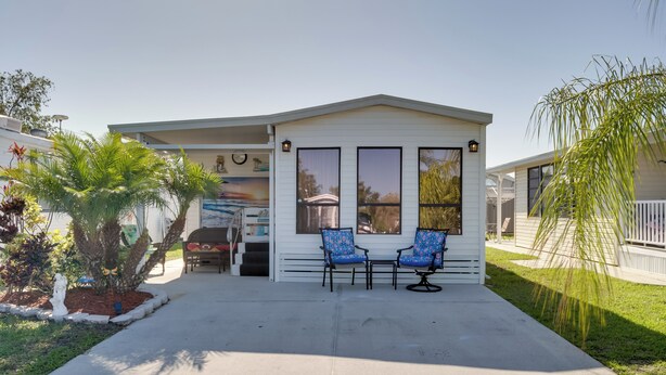A single-story house with a covered porch, two blue patterned chairs, and a small garden with a palm tree. - Resort Pool & Sports Courts! Port Charlotte Home (Port Charlotte)
