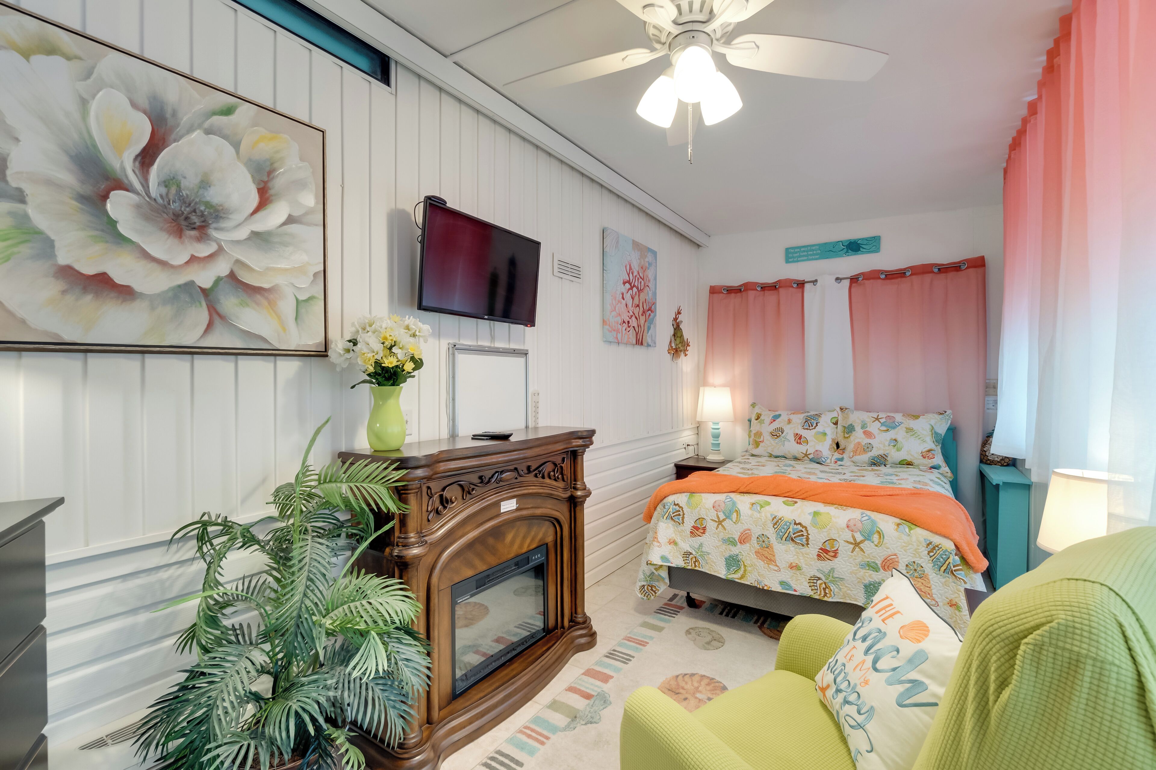 Un dormitorio con cama, televisión, chimenea, planta y un cuadro grande de flores en la pared.
