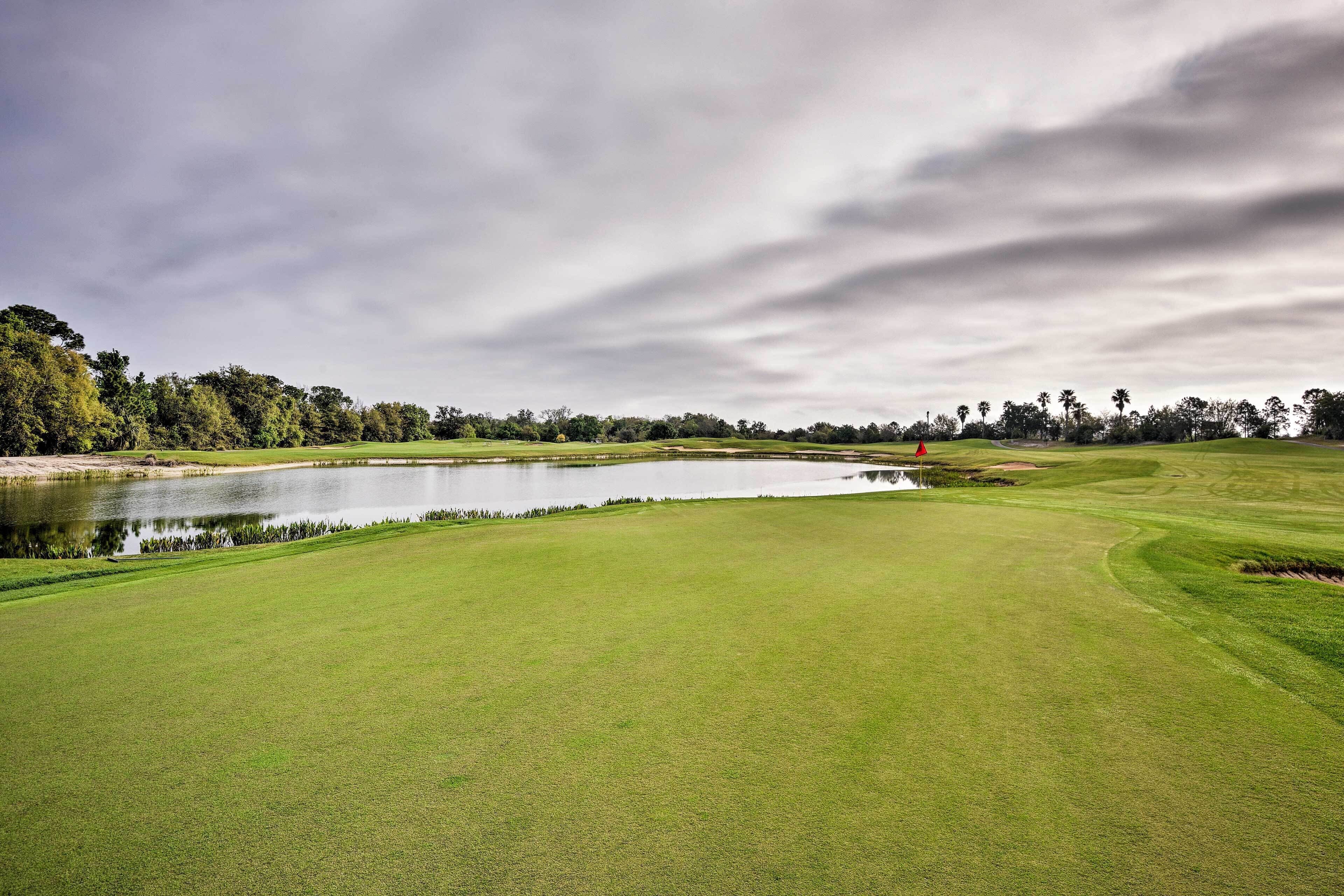 Un parcours de golf avec un étang, des arbres et un ciel nuageux.