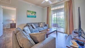 A living room with a gray sectional sofa, a coffee table, a flat-screen TV, and a large window with curtains. - 10 Mi to Disney: Davenport Condo w/ Pool Access! (Davenport)