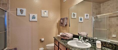 A bathroom with a sink, mirror, and toilet. There are towels and a basket of toiletries.