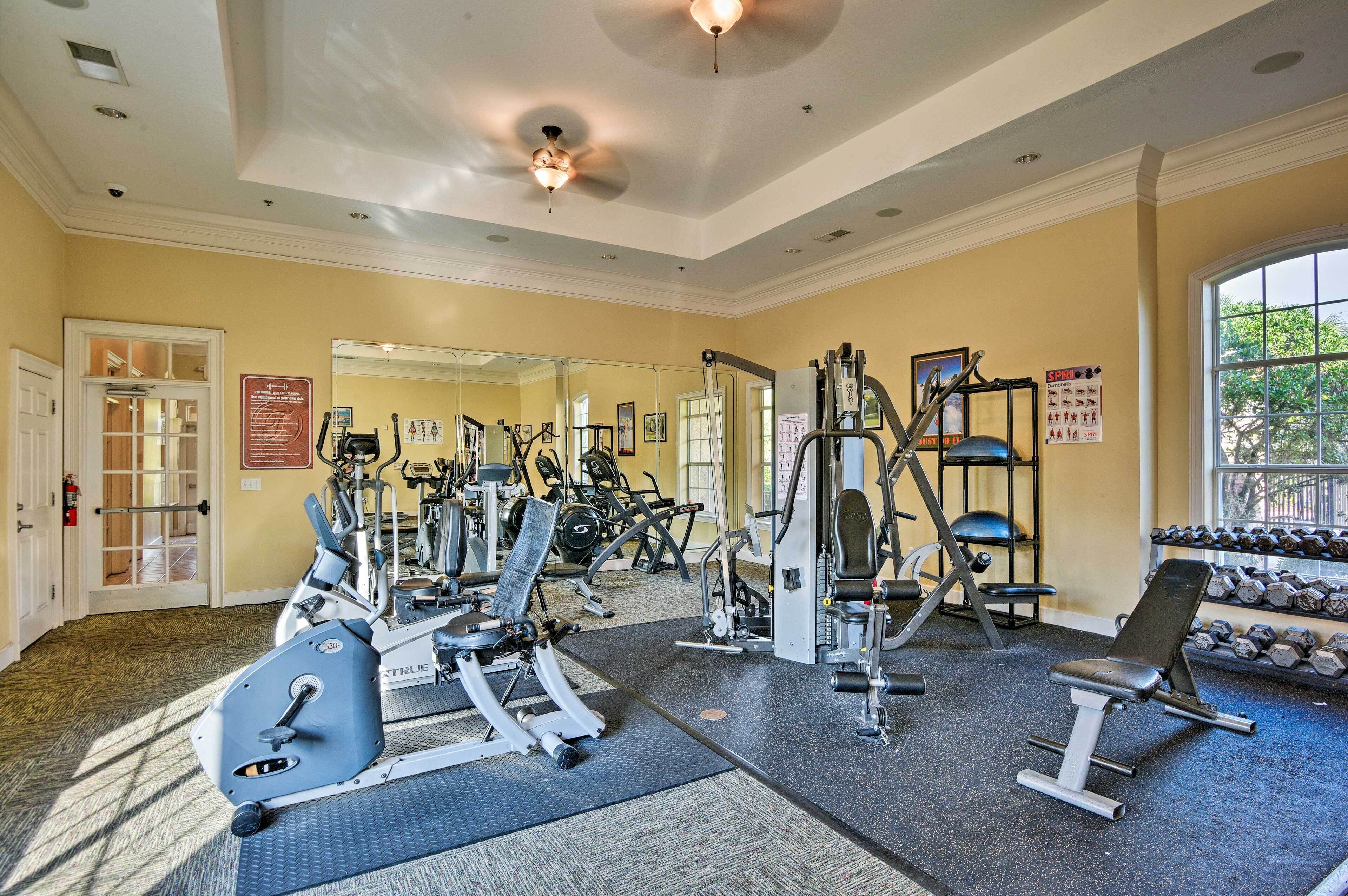 A gym with various exercise equipment, a mirror, and a window with a view of trees.