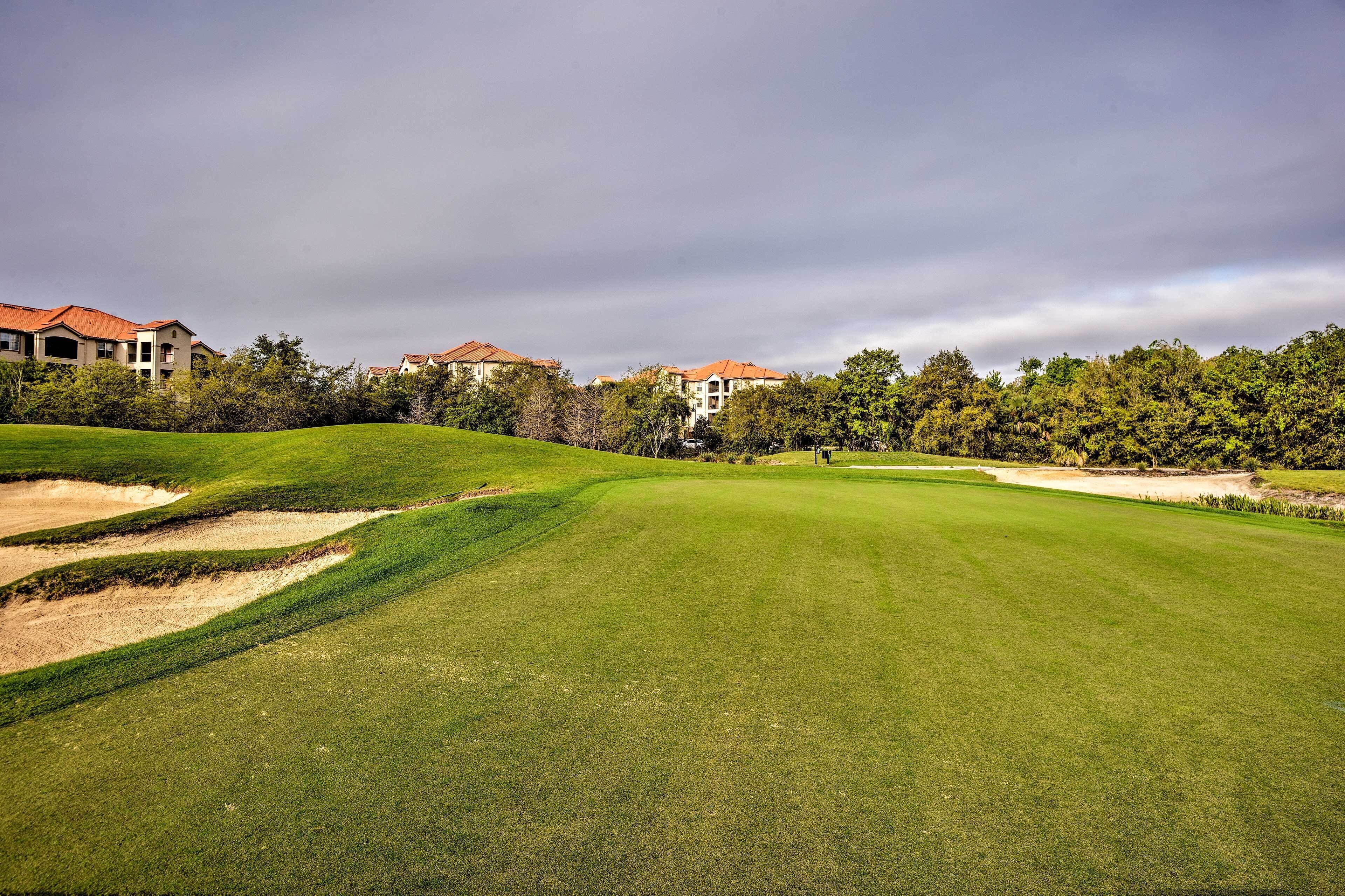 En golfbana med välskött gräs, sandbunkrar och bostadshus som bildar en bakgrund.