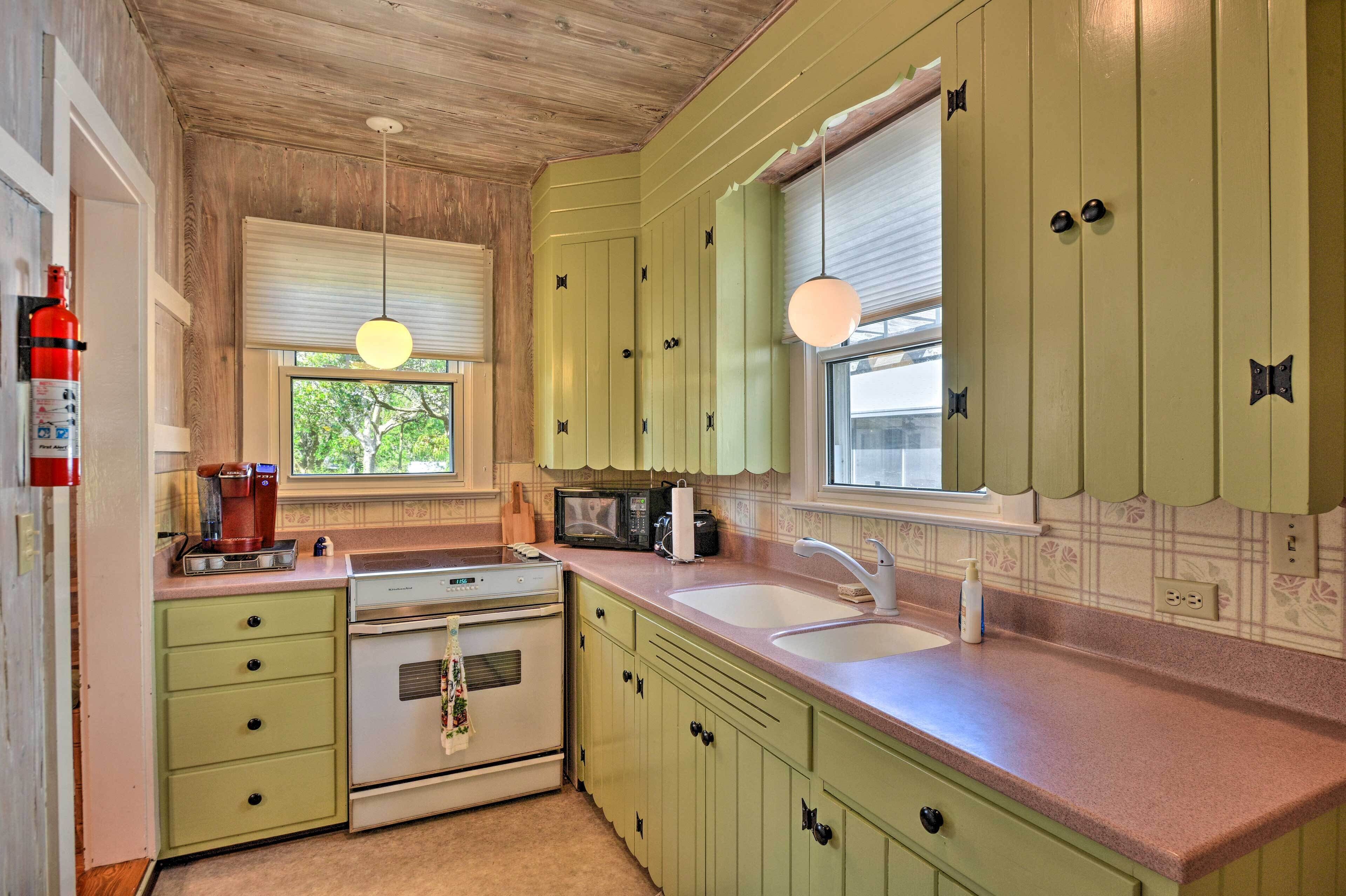 A kitchen with green cabinets, a microwave, a stove, and a sink.