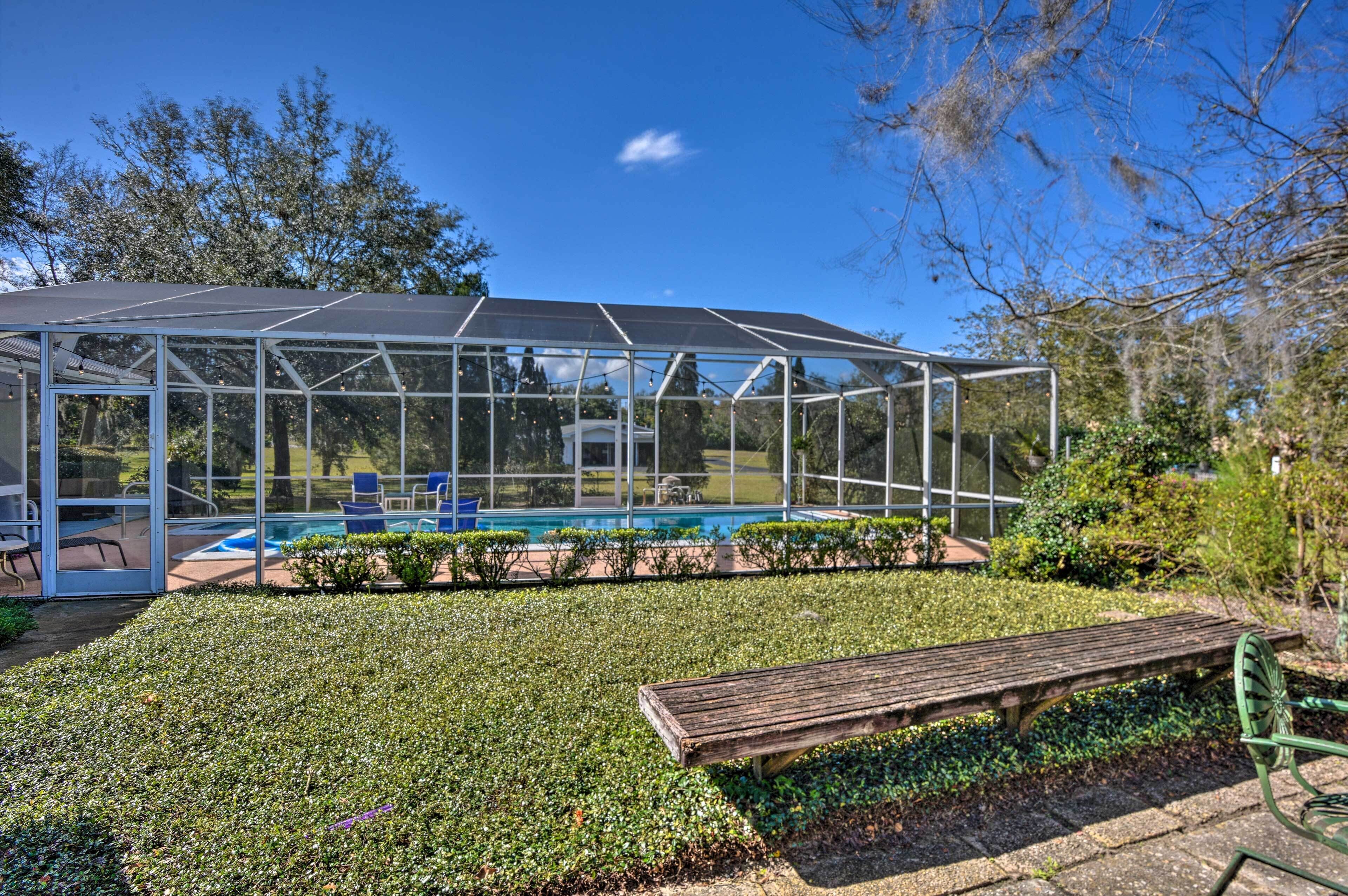A greenhouse structure with a glass roof, a pool, and a wooden bench in a landscaped garden.
