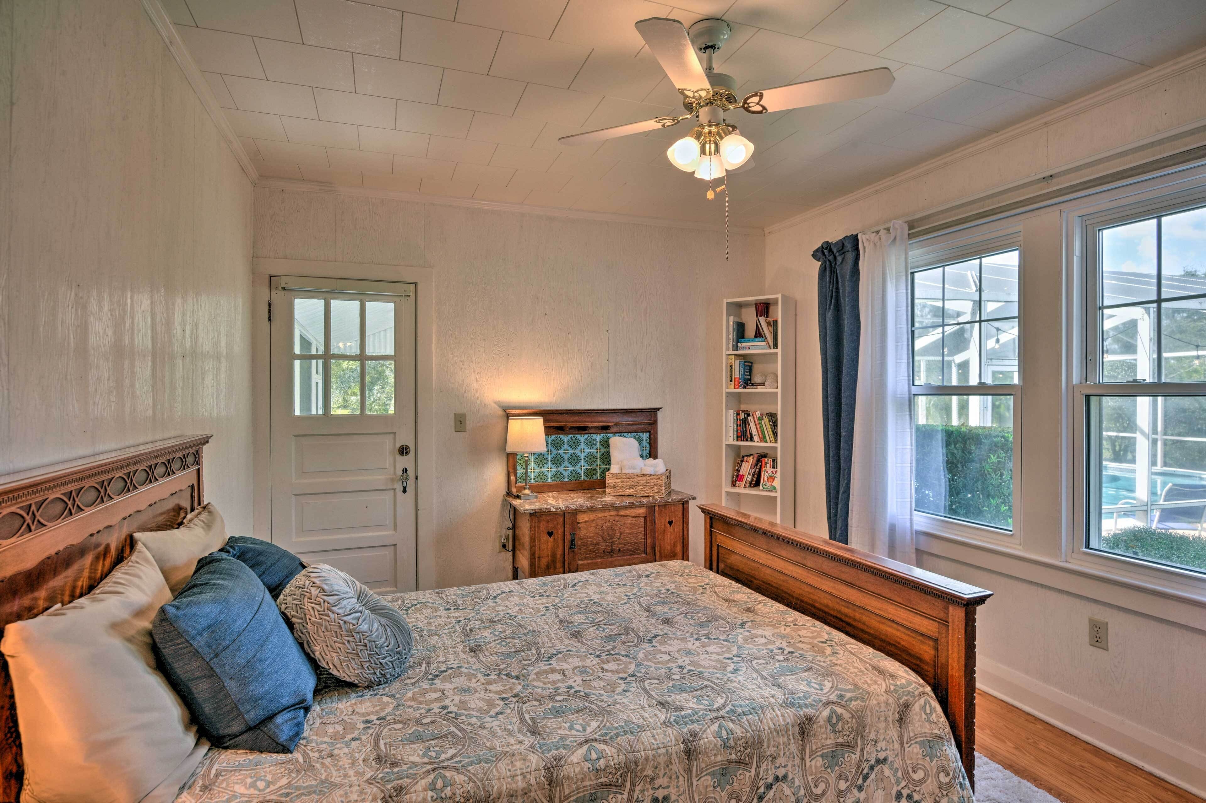 A bedroom with a bed, a dresser, a bookshelf, a window, and a ceiling fan.