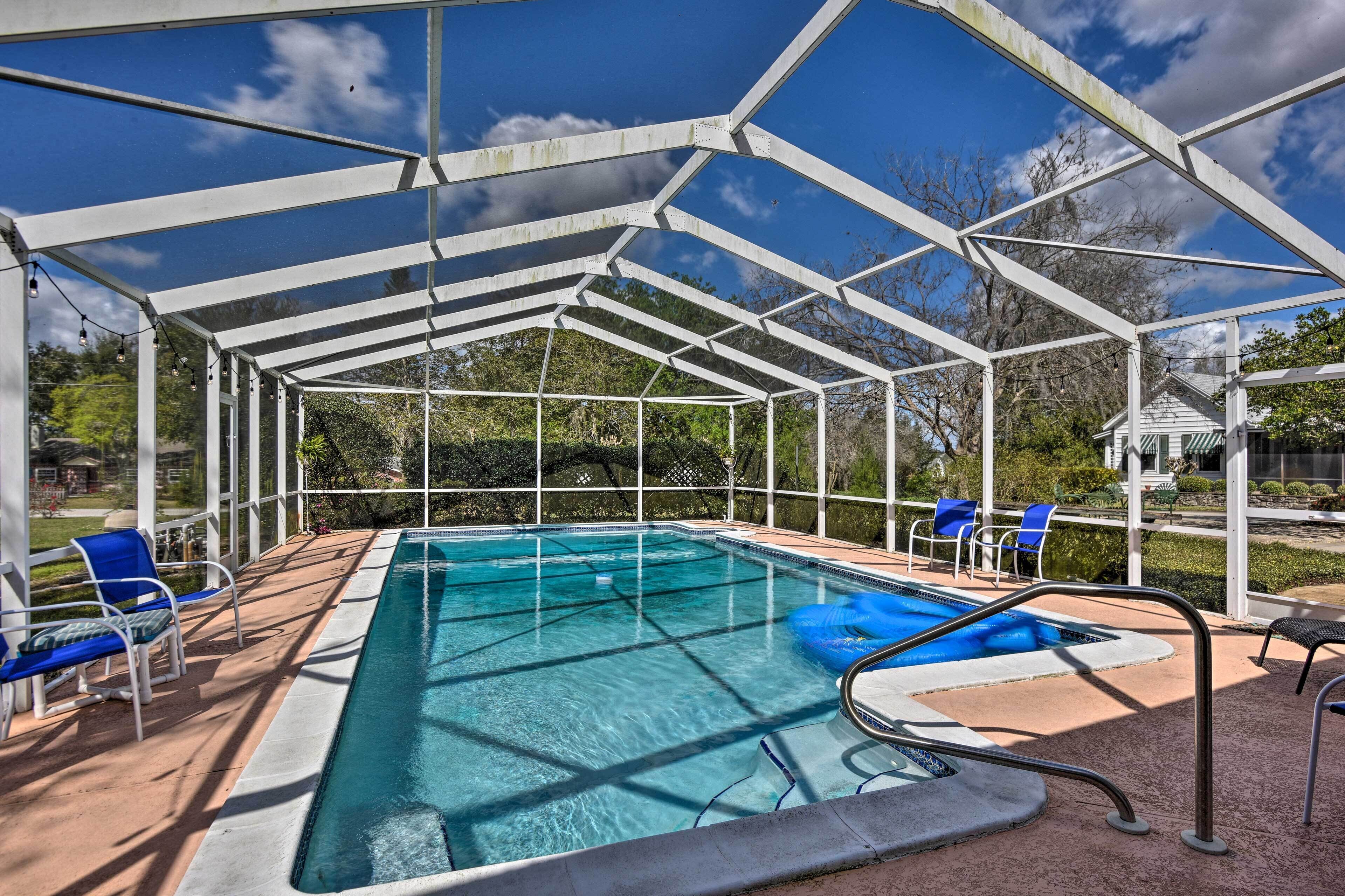 A covered swimming pool with clear blue water, surrounded by white metal beams and blue chairs.